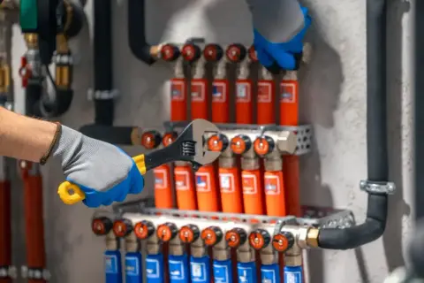 Instalator dokręca kluczem elementy systemu ogrzewania podłogowego, pokazując, jak podłączyć rozdzielacz do grzejników.