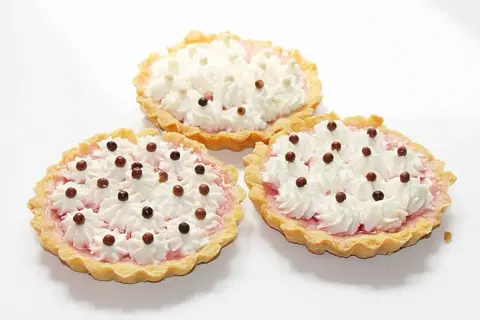 Trzy apetyczne tartaletki z owocami i galaretką, ozdobione bitą śmietaną i czekoladowymi kuleczkami.