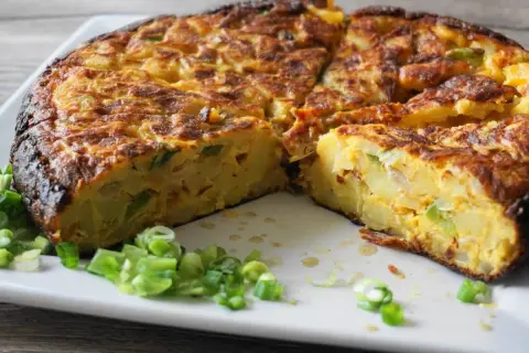 Pyszna tortilla de patatas, pokrojona na kawałki, z zieloną cebulką na talerzu.