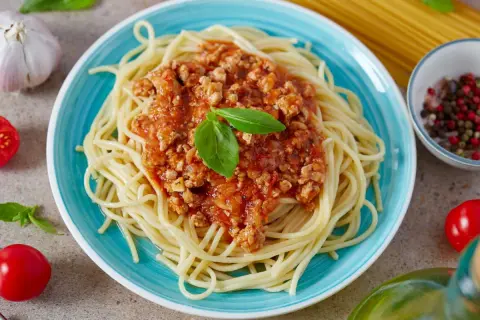 Pyszne spaghetti z sosem bolońskim, idealne, gdy zastanawiasz się, jak zrobić sos do spaghetti. Podane na niebieskim talerzu, z bazylią i pomidorkami.