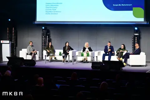Panel dyskusyjny z udziałem ekspertów na scenie, siedzących na białych sofach.