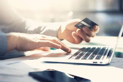 Dłonie wpisują dane karty na laptopie, planując płatność za granicą. Sprawdź prowizję za płatność kartą za granicą PKO BP.