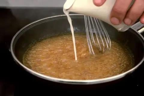 Se añade líquido a una salsa burbujeante en una sartén mientras se bate, para espesar salsa con maicena.