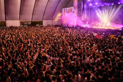 Multitud vibrante en concierto, con luces de escenario y carteles. Se aprecia la **autorización menores espacio Zity** en un cartel.