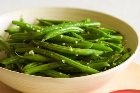 Fagiolini freschi saltati in padella con aglio e pepe, serviti in una ciotola di legno.