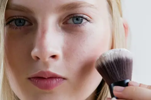 Blondynka nakłada puder transparentny pędzlem. To sekret naturalnego wykończenia makijażu.