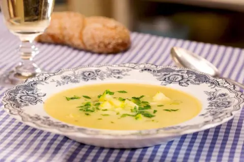 Eine cremige Zucchini-Suppe mit frischer Petersilie in einer eleganten Schüssel, daneben ein Glas Weißwein und ein Brot.