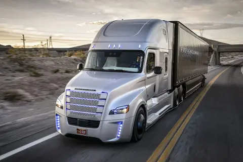 Un camion américain nez plat argenté roule sur une route déserte au coucher du soleil.