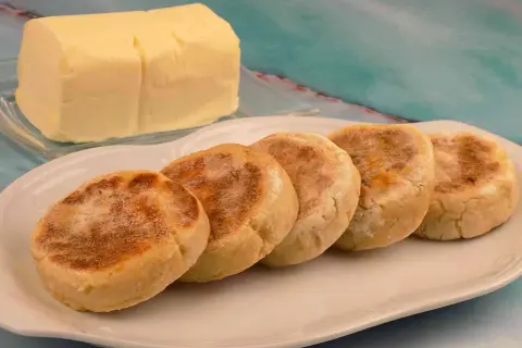 Pięć angielskich muffinek na talerzu, obok kostka masła. Idealne na śniadanie, jak u naszych moskali.