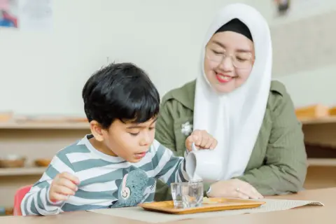 A child practices pouring water in a Montessori classroom, learning practical life skills inspired by nature.