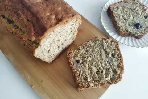 Domowy chlebek bananowy z kawałkami orzechów i rodzynek, pokrojony na desce.