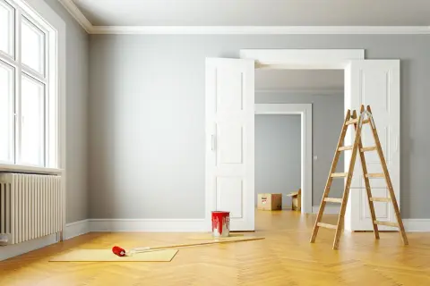 Leere Wohnung bereit zur Renovierung. Ein Farbeimer und eine Leiter stehen bereit, um die Wände zu streichen.