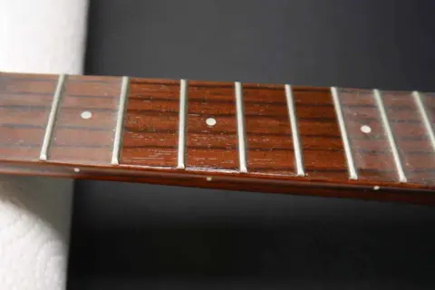 Nahaufnahme des Griffbretts einer Ukulele mit Bundstäbchen und Saiten. Perfekt für Anleitungen zum Ukulele Saiten wechseln.