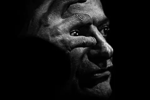 Intensywny portret w czerni i bieli, gdzie dłoń zakrywa oko, przywołuje mroczny styl antoine d'agata.