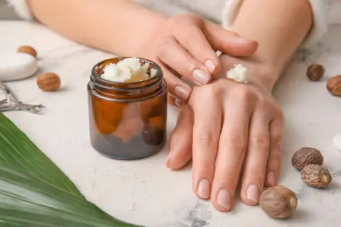 Mani che applicano burro di karitè, con noccioli e un barattolo. Informazioni su burro di karitè: controindicazioni.