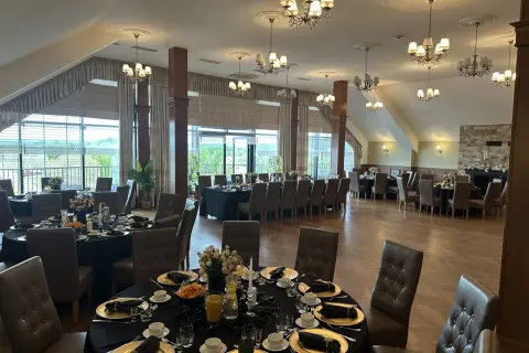 Elegancka sala bankietowa w ośrodku jeździeckim Lando, przygotowana na przyjęcie. Stoły nakryte czarnymi obrusami, złote talerze i eleganckie krzesła.