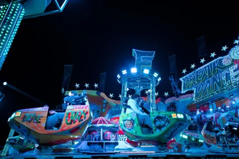 Bunte Fahrgeschäfte und Lichter auf dem Berliner Volksfest. Menschen genießen die Nacht auf dem "Break Dance".