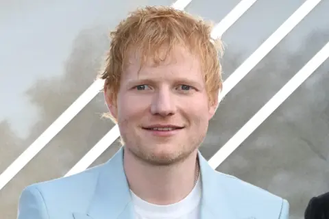 Ed Sheeran, der aus Halifax, England, stammt, lächelt in einem hellblauen Anzug.