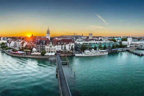 Friedrichshafen heute: Sonnenuntergang über dem Bodensee, mit Schiffen im Hafen und der Promenade.