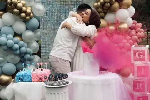 Para świętuje płeć dziecka. Różowy dym unosi się, a balony w kolorach niebieskim i różowym sugerują balon chłopiec czy dziewczynka.