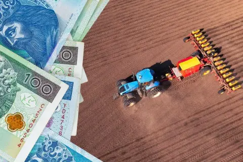Pieniądze i niebieski traktor z siewnikiem na polu. Czy to symbol rolnictwa i podatku rolnego?