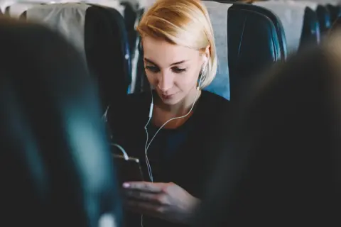 Kobieta w słuchawkach korzysta z telefonu, ciesząc się internetem w samolocie.