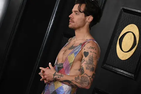 Harry Styles mit vielen Tätowierungen, die als Inspiration für Tattoo Ideen Mann dienen. Ein Herz, ein Schiff und Rosen sind zu sehen.
