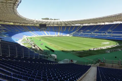 Puste trybuny stadionu Lazio, z zieloną murawą i bramkami, czekają na kibiców.