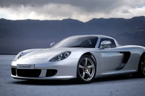 Srebrny Porsche Carrera GT na pustkowiu, z górami w tle.