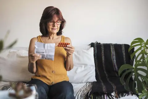 Kobieta czyta ulotkę leku, trzymając opakowanie tabletek. Szuka informacji o lekach na menopauzę bez recepty.