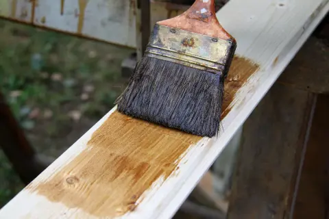 Application d'une lasure blanche sur une planche de bois. Le résultat avant/après est visible sur la surface traitée.
