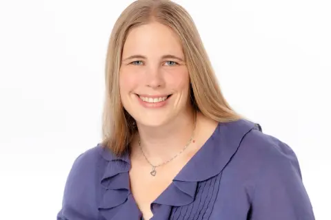 Lächelnde Frau mit blonden Haaren und blauen Augen, trägt eine lila Bluse. Sie könnte eine engagierte studentische Hilfskraft sein.