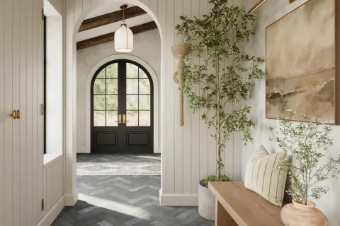 A bright, airy hallway with a dark arched doorway leading outside. A potted tree and bench add warmth to the space.
