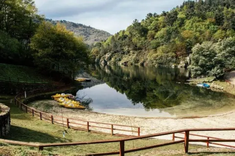 Playa fluvial a Calzada con kayaks amarillos esperando en la arena, rodeada de árboles verdes y un río tranquilo.
