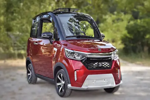 Auto rossa compatta, ideale per la mobilità ridotta, con tetto apribile e dettagli moderni, parcheggiata su una strada sterrata tra gli alberi.