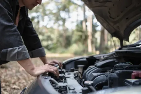 Un homme regarde le moteur de sa voiture qui cale à bas régime, bloqué en pleine nature.