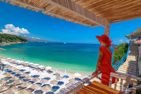 Kobieta w czerwonej sukience podziwia turkusowe morze i plażę z leżakami. Idealne miejsce, by sprawdzić, gdzie najtaniej na wakacje.
