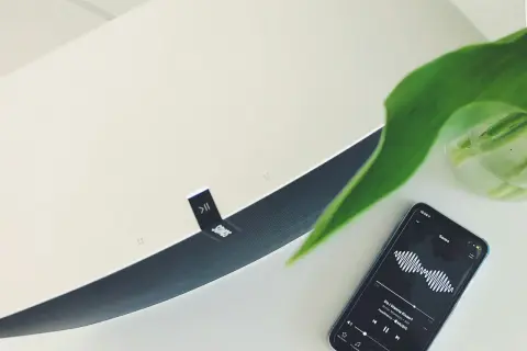 Telefon z aplikacją Sonos i odtwarzaną muzyką, obok głośnik tej marki. To pokazuje, jak działa airplay co to za technologia.