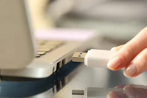 Dłoń wkłada biały pendrive do portu USB laptopa, rozpoczynając nagrywanie danych.