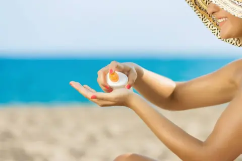 Mujer con sombrero aplicando crema solar en la mano. ¡No dejes que la crema solar caduca te arruine el día en la playa!