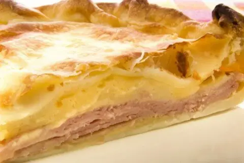 Rebanada de tarta de jamón y queso, con capas de masa dorada, jamón rosado y relleno cremoso. ¡Un bocado delicioso!