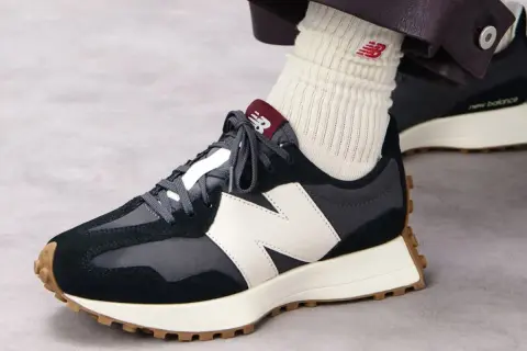 Sznurowanie butów New Balance. Ciemne sneakersy z białym logo N i brązową podeszwą.