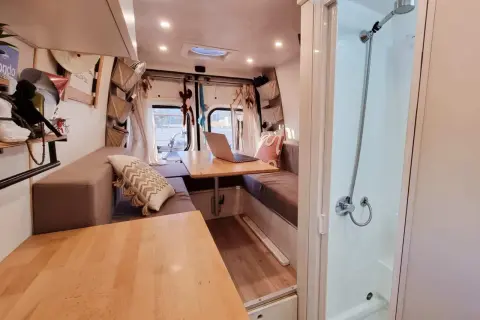 Interno camper con divanetti, tavolo e un box doccia in legno fai da te.