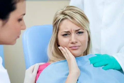 Kobieta cierpi na ból zęba po zatruciu. Dentysta i asystentka próbują jej pomóc.