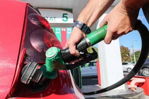 Remplissage d'une voiture thermique rouge à la station-service. Le pistolet vert est inséré dans le réservoir.