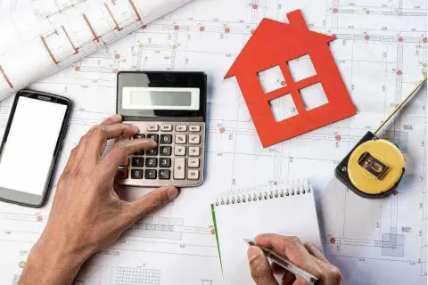 Manos calculando presupuesto para obras de reforma. Planos, calculadora, cinta métrica y casa roja.