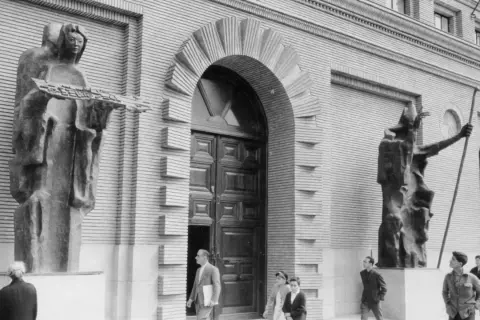Esculturas flanquean la entrada del ayuntamiento en la Plaza del Pilar. Figuras abstractas de bronce, una sostiene un modelo de ciudad.