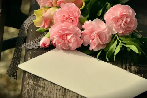 Bukiet różowych kwiatów, koronka i pusta kartka na drewnianym tle.