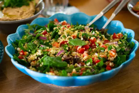 En stor blå skål fylld med ett färgglatt tabbouleh recept med bulgur, tomater, lök och färska örter.