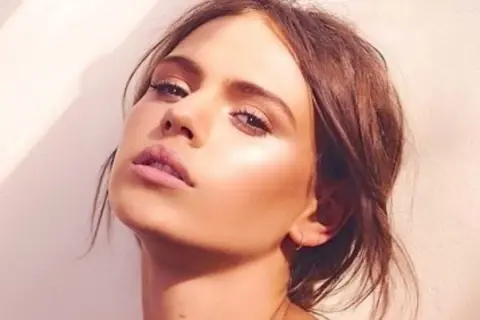 Visage d'une jeune femme au maquillage lumineux, elle pose avec un regard intense. Peut on bronzer avec du maquillage ? Sa peau semble éclatante.